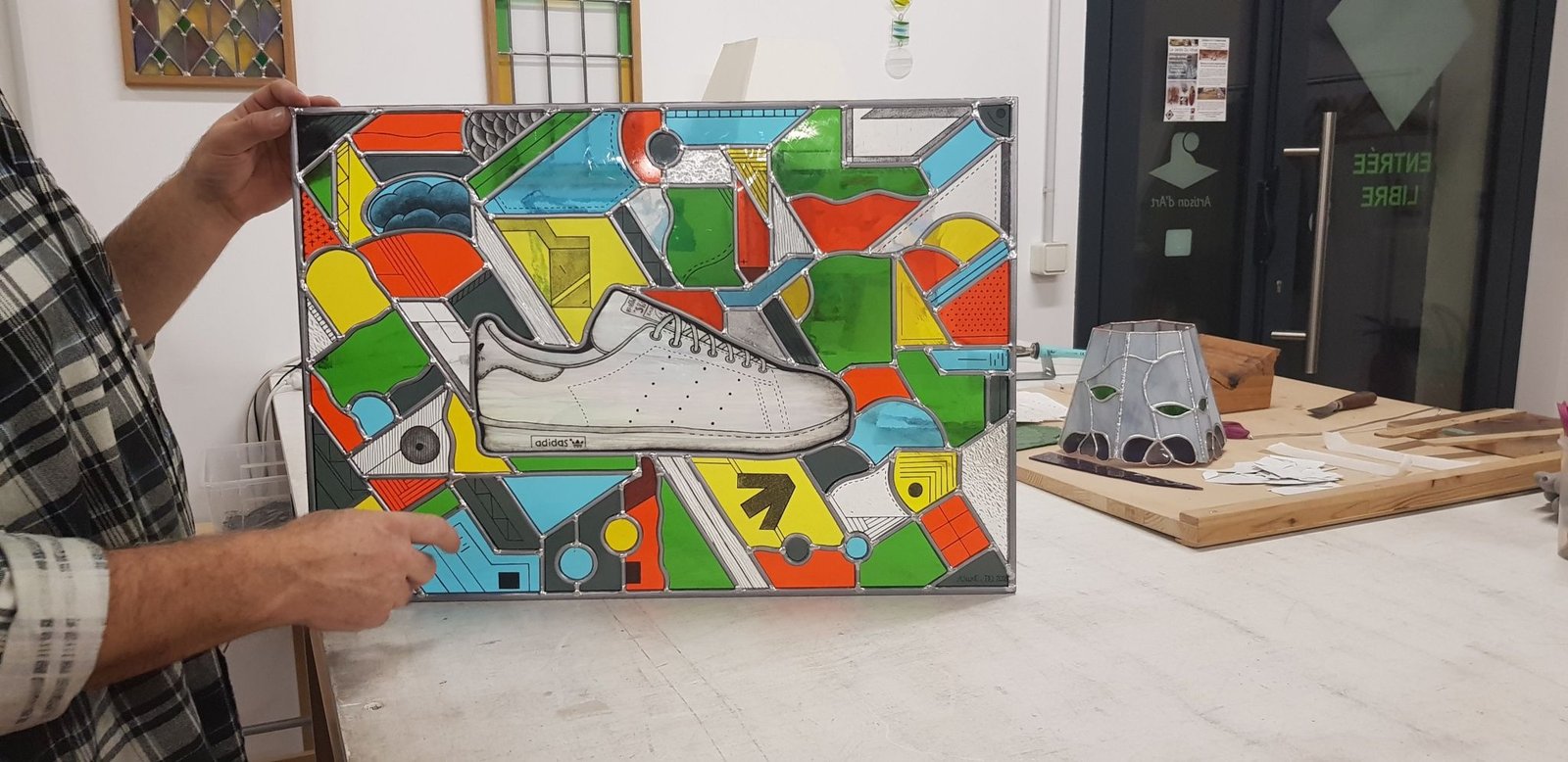 Le vitrail Stan Smith terminé, tenu à la main dans l'atelier.