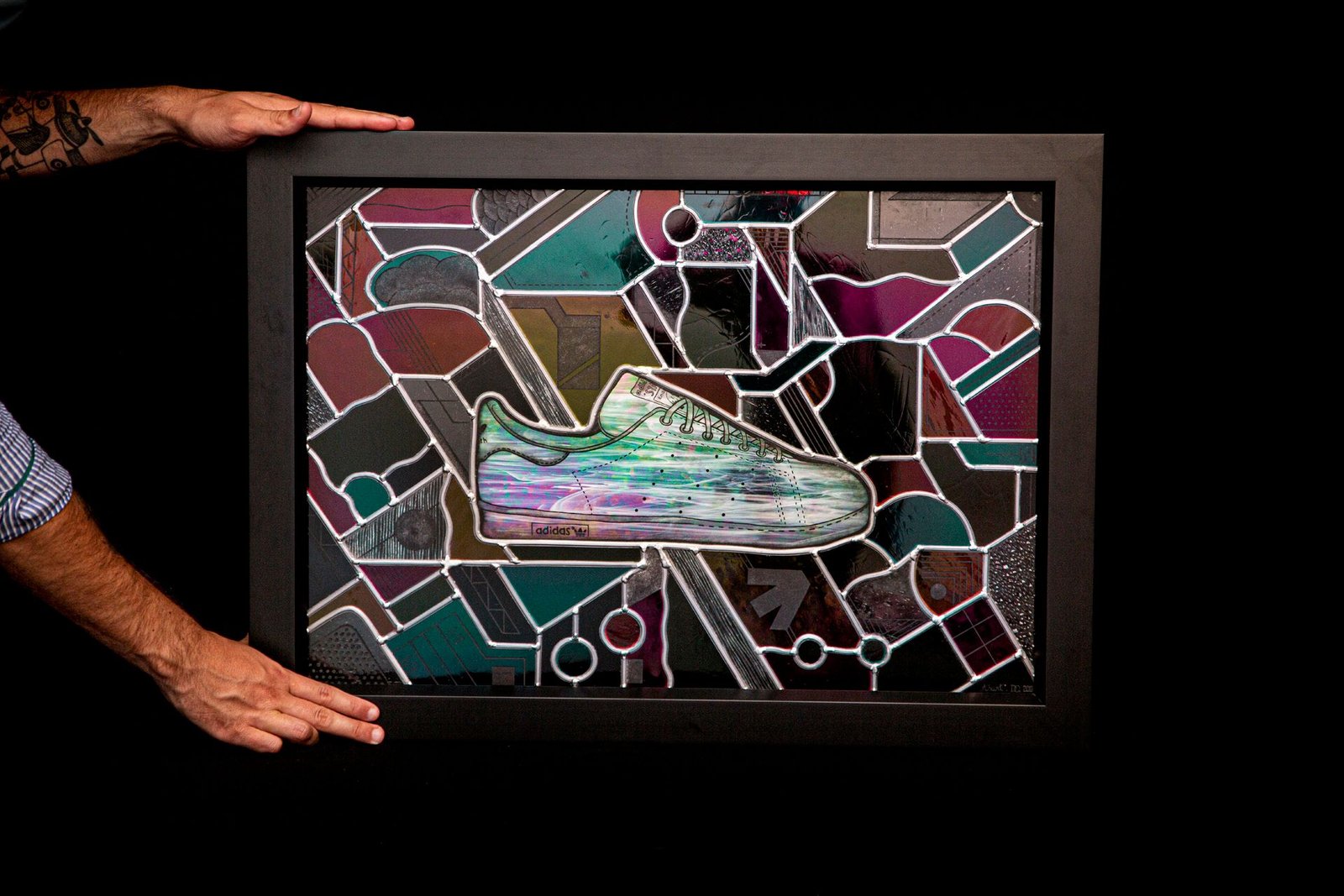 The framed window lit from the front: purple and green reflections on the glass and the iridescent Stan Smith.