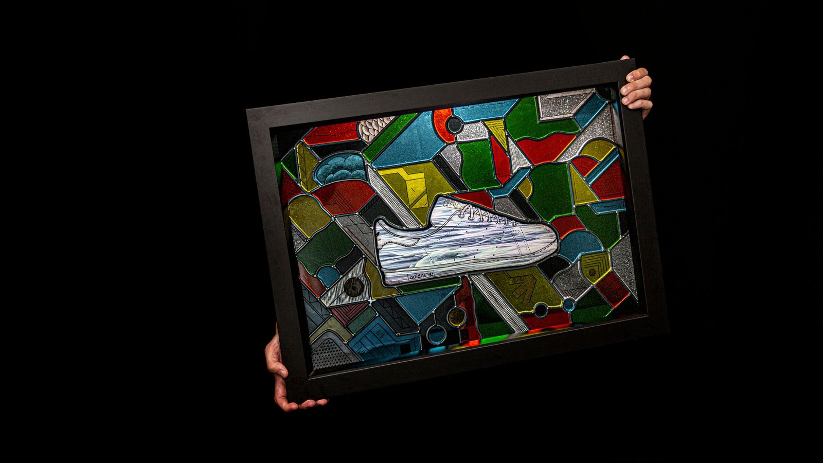 The framed window held at an angle in the dark: the iridescent Stan Smith among the coloured pieces.